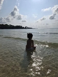 Eine dreijährige sitzt in den sanften Wellen von Koh Samet