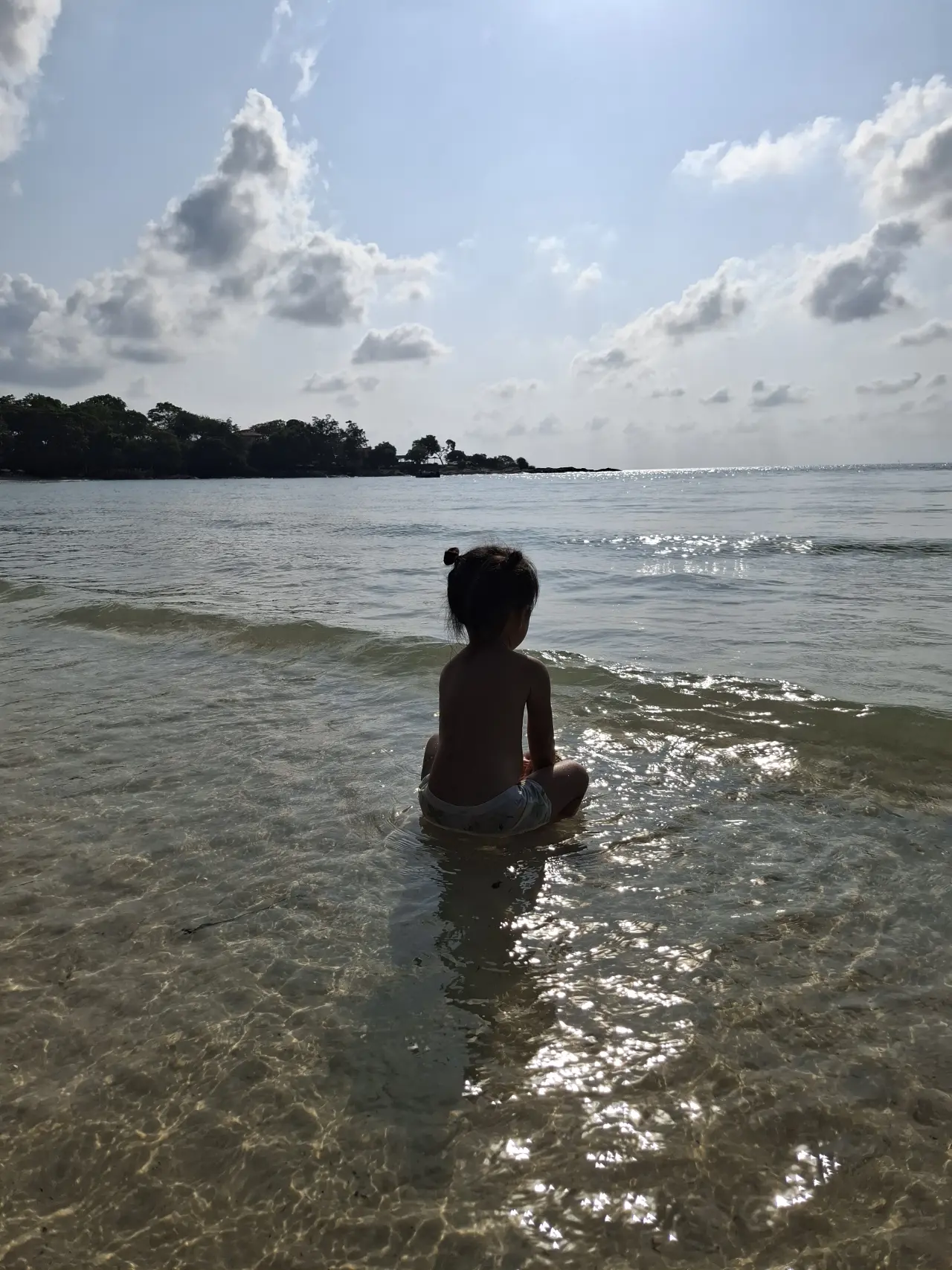 Eine dreijährige sitzt in den sanften Wellen von Koh Samet