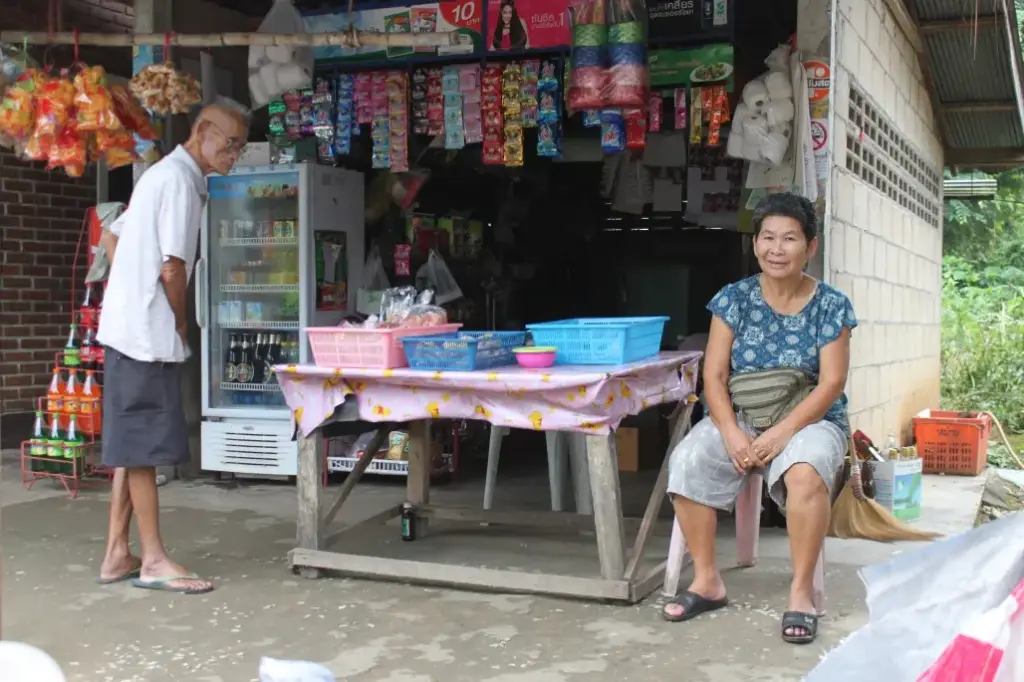 Eine alte Frau sitzt vor einer Garage, die als Laden dient. Bei Mae Sai in Nordthailand.